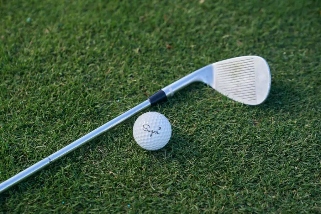 A golf club and golf ball with sugar written on it lying on the grass 