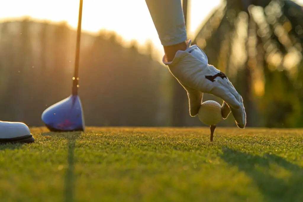 A golfer off-screen placing a ball on a tee