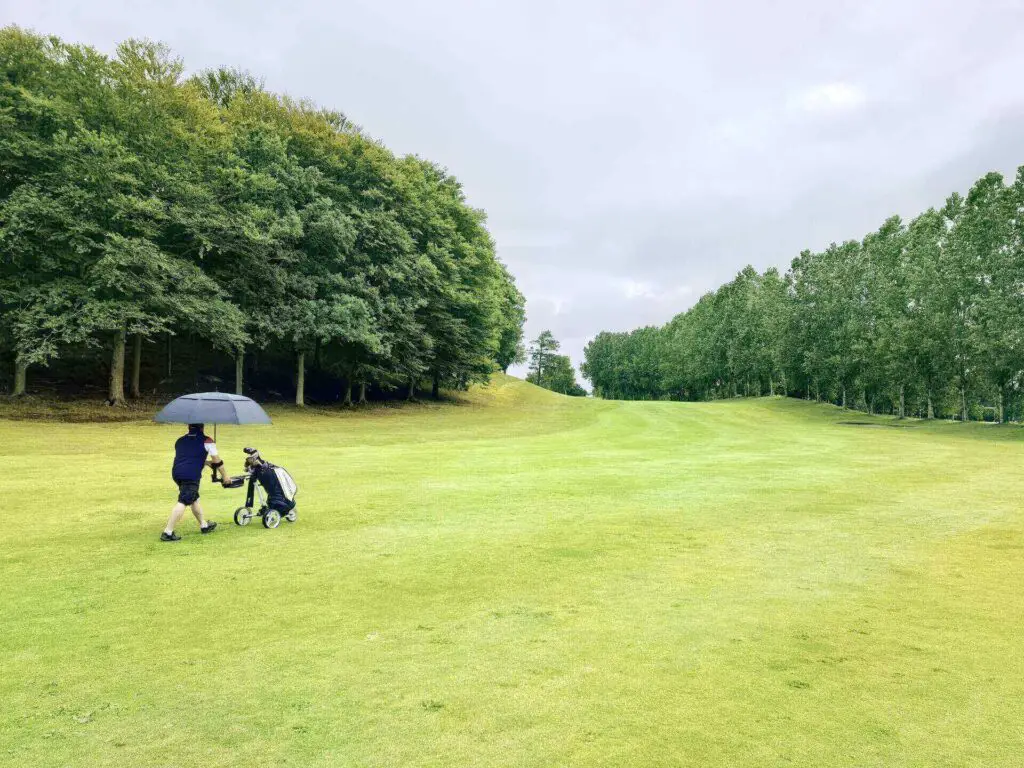 A man with an umbrella pushing a golf push cart