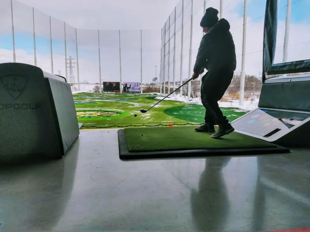 A player swinging his club and hitting the ball at a TopGolf driving range