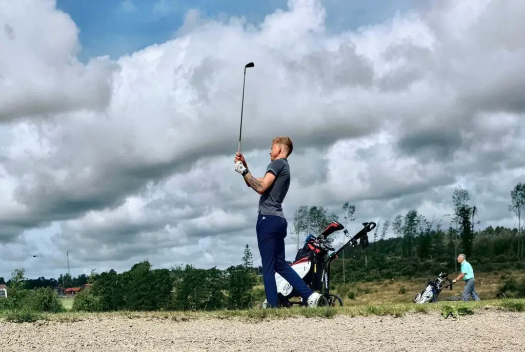 A man golfing next to a golf push cart