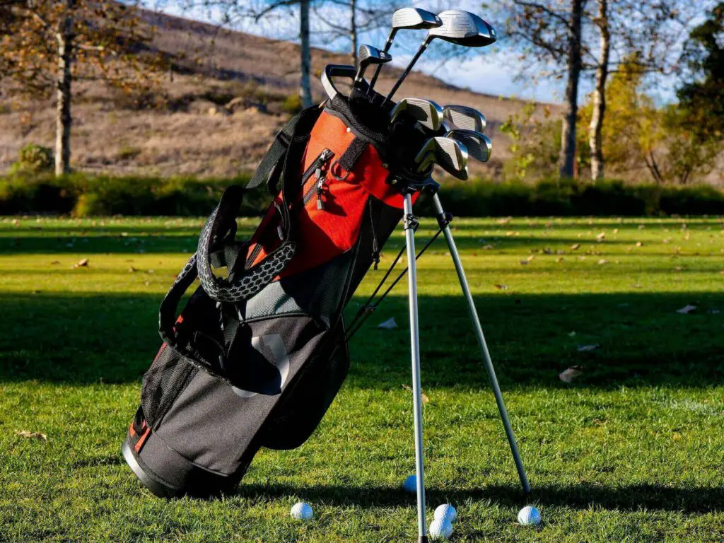 A stand bag full of golf clubs, surrounded by golf balls on the green