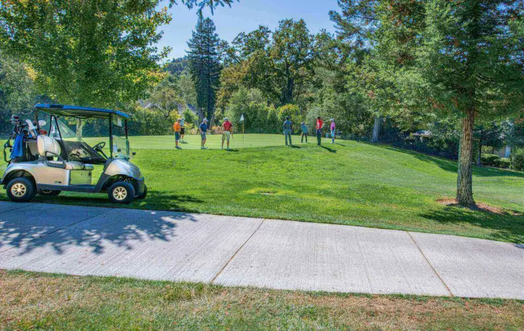 A golf cart and a bunch of players near a golf hole