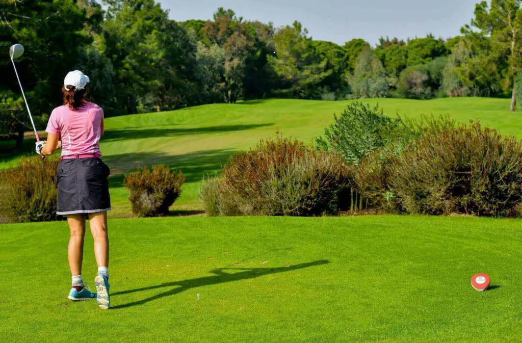 A woman in a pink shirt swinging a golf club
