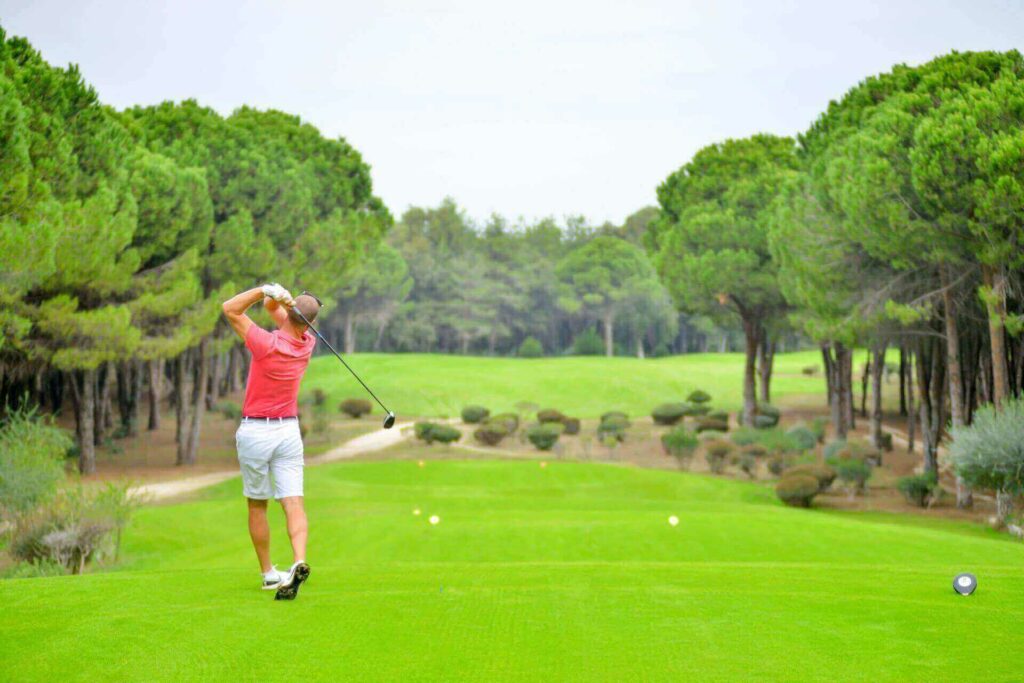A man in a pink shirt and white pants swinging a golf club