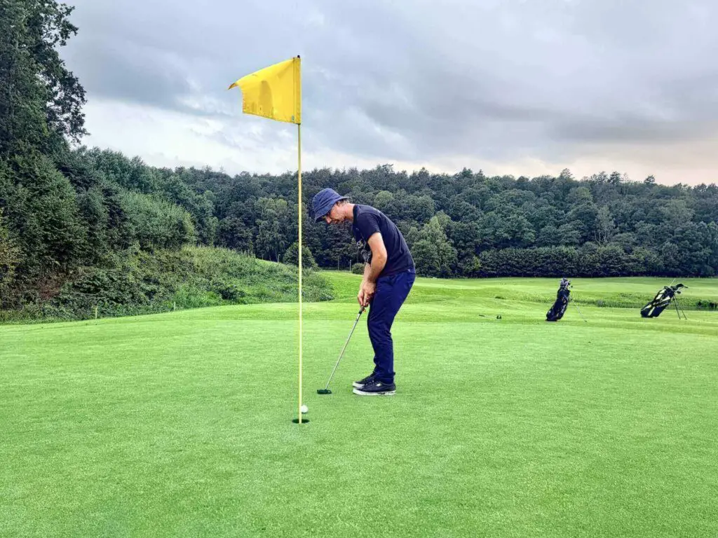 A man with a cap hitting a golf ball into a hole