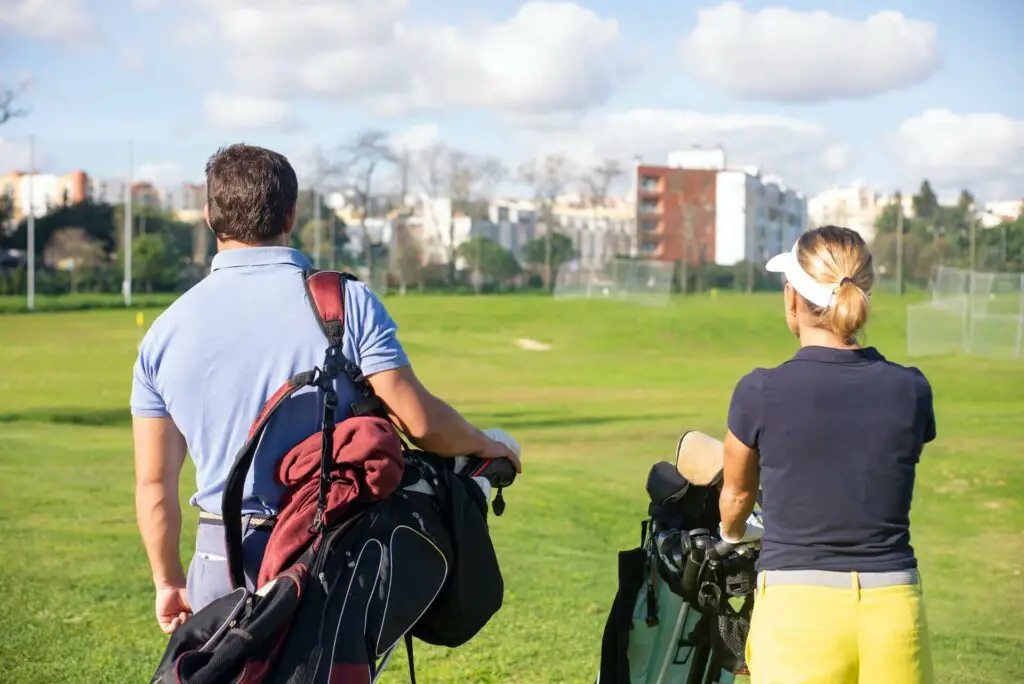 Two people carrying golf bags on their shoulders