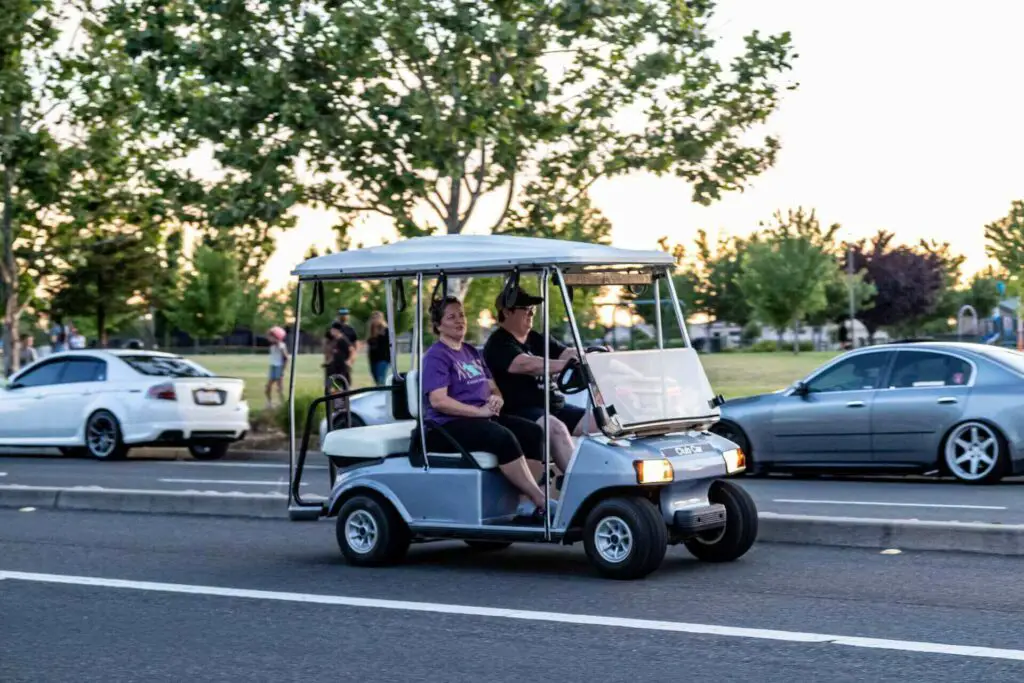 A couple of people riding a golf cart on a public road