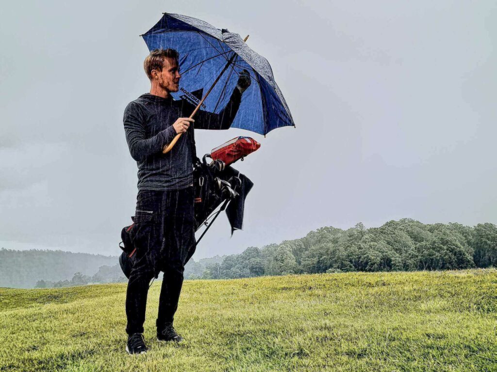 A man holding his umbrella while carrying a golf bag