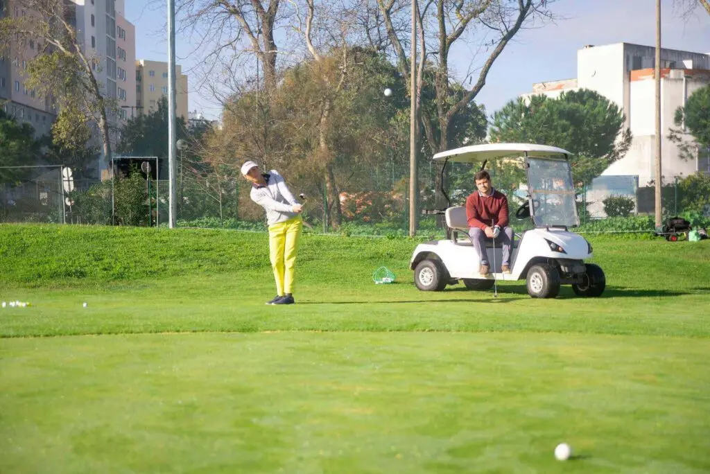 A woman striking a ball and a man sitting in a cart watching